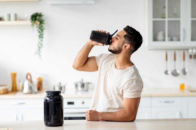 Young Arab guy drinking protein shake from bottle at kitchen, copy space. Body care concept Your Protein Shake Safety Questions Answered: Finding Clean, Non-Toxic Alternatives